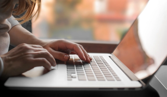 Person looks at a laptop screen. Their hands are positioned to type on the keyboard.