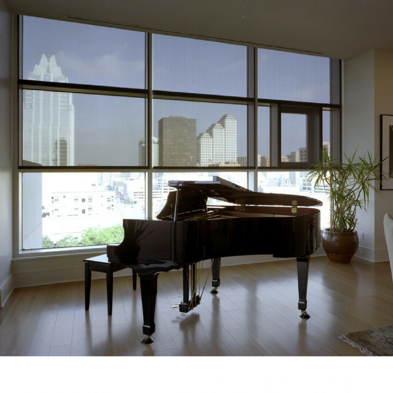 Roll-up solar screens installed in an Austin apartment, providing shade to a piano.